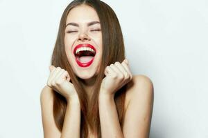 Woman with bare shoulders laughs with his mouth wide open and hands near his face lipstick photo