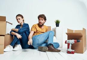 A man and a woman are sitting on the floor indoors near the couch and moving boxes photo