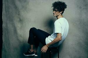 curly-haired guy sitting on a chair with glasses fashion studio photo