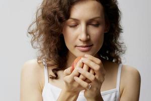 Happy curly beautiful woman in basic white t-shirt sniffing an apple enjoyed smell of fruit posing isolated on over white background. Natural Eco-friendly products concept. Copy space photo