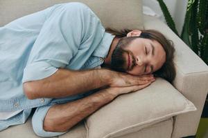 un hombre dormido en el sofá durante el día es cansado y relajado después estrés y sensación malo. estrés a trabajar, pobre dormir y salud problemas foto