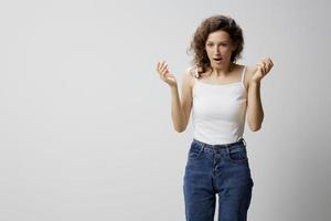 Confused shocked curly beautiful woman in basic white t-shirt raise hands up open mouth posing isolated on over white background. People Emotions Lifestyle. I can not believe it concept. Copy space photo