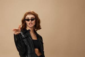 Funny adorable stylish pretty redhead lady in leather jacket sunglasses posing isolated on pastel beige studio background. Copy space Banner Offer. Over black concept. Fashion Cinema. Seasonal Sale photo