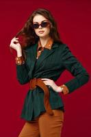 pretty woman holding hair fashionable suit and sunglasses luxury red background photo