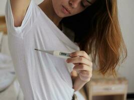 mujer en blanco camiseta comprobación el temperatura con un termómetro foto