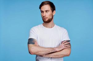 hermoso hombre en blanco camiseta tatuajes en su brazos recortado ver azul antecedentes foto