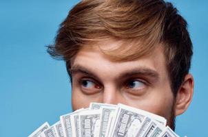 a man with a wad of money covers his face close-up blue background photo