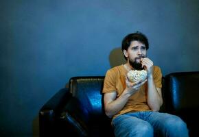 solitario hombre en el noche en el sofá en frente de el televisión y palomitas de maiz en un plato foto