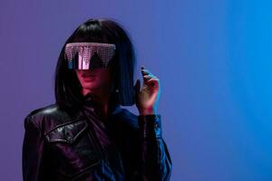 Shocked awesome brunet woman in leather jacket specular sunglasses open mouth look aside posing isolated in blue violet color light background. Neon party Cyberpunk concept. Copy space. Good offer photo