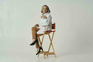 an elderly woman in a white shirt sits on a chair posing photo