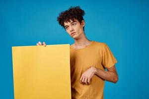 guy with curly hair holding a yellow poster in his hands advertising photo