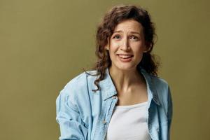 Emotional upset confused curly beautiful female in jeans casual shirt looks at you posing isolated on over olive green pastel background. Being Yourself. People Lifestyle emotions concept. Copy space photo