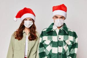 A cute young couple in medical masks are standing next to a Santa hat close-up photo