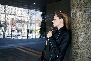 mujer en cuero chaqueta en el calle en el ciudad y edición Gafas de sol en el antecedentes foto
