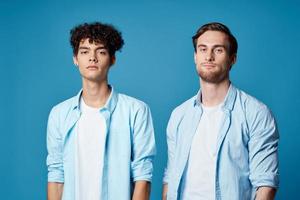 two friends in identical shirts and a t-shirt gesturing with their hands on a blue background photo