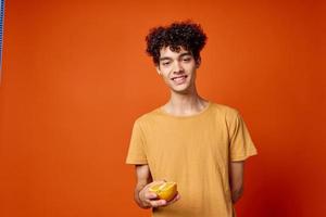 alegre Rizado chico en un amarillo camiseta naranjas en su manos rojo antecedentes foto
