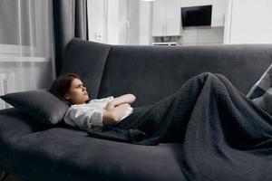 offended woman lies on the sofa in the room under a warm blanket photo