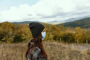 beautiful woman tourist in a medical mask on a meadow in the mountain photo