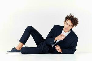 a man with curly hair lies in a suit on the floor in a bright room and sneakers style photo