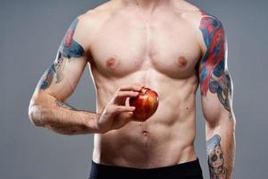 young man with apple and pumped up torso biceps man tattoo gray background cropped view photo