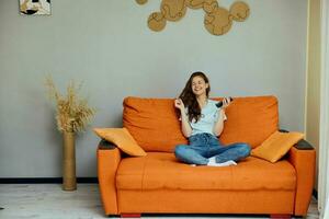 retrato de un mujer chateando en el naranja sofá con un teléfono inteligente inalterado foto
