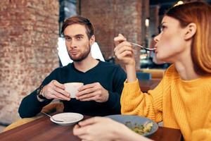 mujer teniendo cena a un mesa en un café y un hombre con un taza de café en el antecedentes foto