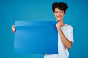 Cheerful guy with curly hair and blue mockup poster advertising photo