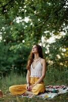 A young hippie woman meditates in nature in the park, sitting in a lotus position on her colorful plaid and enjoying harmony with the world in eco-clothing in the autumn photo