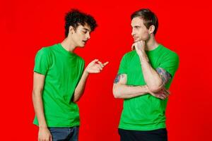 two men in green t-shirts are standing side by side communication photo