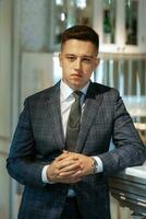 portrait of a groom in a gray plaid suit with a tie in a light bar photo