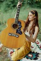 hippie mujer eco simpático jugando guitarra sonrisas y canto canciones en naturaleza sentado en un tartán por el lago en el noche en el puesta de sol luz de sol. un estilo de vida en armonía con el cuerpo y naturaleza foto