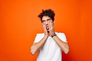 guy in a white t-shirt with curly hair holding his head emotions orange background photo