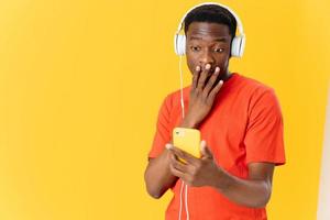 un hombre de africano apariencia en un naranja camiseta vistiendo auriculares con un teléfono en su manos foto