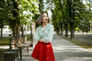 pretty blonde in red skirt outdoors in the park green trees photo