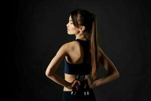 woman with dumbbells in hands dark background workout inflated muscles photo