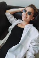 A woman lying on the couch with her glasses on and wriggling photo
