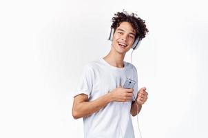 gracioso chico con Rizado pelo en un blanco camiseta escucha a música tecnología entretenimiento foto