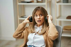 cauteloso joven rubia estudiante dama en calentar suéter elimina auriculares escucha a externo sonidos mira aparte sentado en Sillón a moderno hogar. música hora relajante frio lista de reproducción concepto. Copiar espacio foto