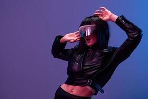 Excited pretty awesome brunet woman in leather jacket trendy specular sunglasses open mouth leans back posing isolated in blue violet color light background. Neon party Cyberpunk concept. Copy space photo