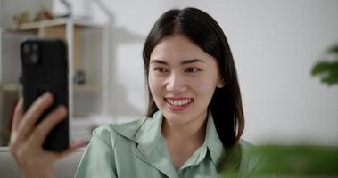 Handheld slow motion shot, Asian young woman talking during use smartphone to video call with someone, she smile and laugh with happy in living room at home