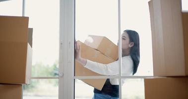 portátil médio tomada, ásia jovem mulher carregando caixas e aberto vidro porta para mover para dentro Novo casa video