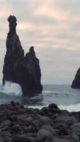 Large rock formations in the sea as waves crash on a stony shore video