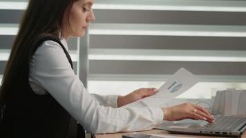 côté vue de calme concentré femme travail en utilisant papier les documents et portable séance dans le moderne bureau. video
