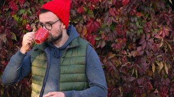 Man in a red cap with a cup in his hands drinking tea or coffee outdoors. Coffee break. video