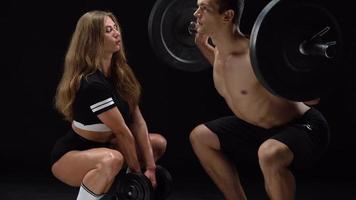 Athletic man and woman doing exercise on the shoulders with elastic bands on a black background in studio video