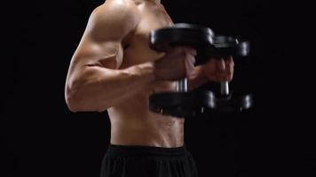 Man flexes his hands with dumbbells, training his shoulders on a white background in the studio video