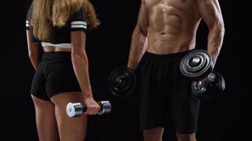 Athletic man and woman doing exercise on the shoulders with elastic bands on a black background in studio video