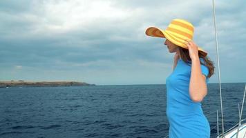 Woman in a yellow hat and blue dress girl rests aboard a yacht near the lighthouse on summer season at ocean video