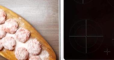 cutlets rolled in flour on a wooden Board on the background of the included kitchen stove top view. video