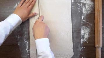 Women's hands cut the dough with a knife, on the surface of the table. The view from the top video